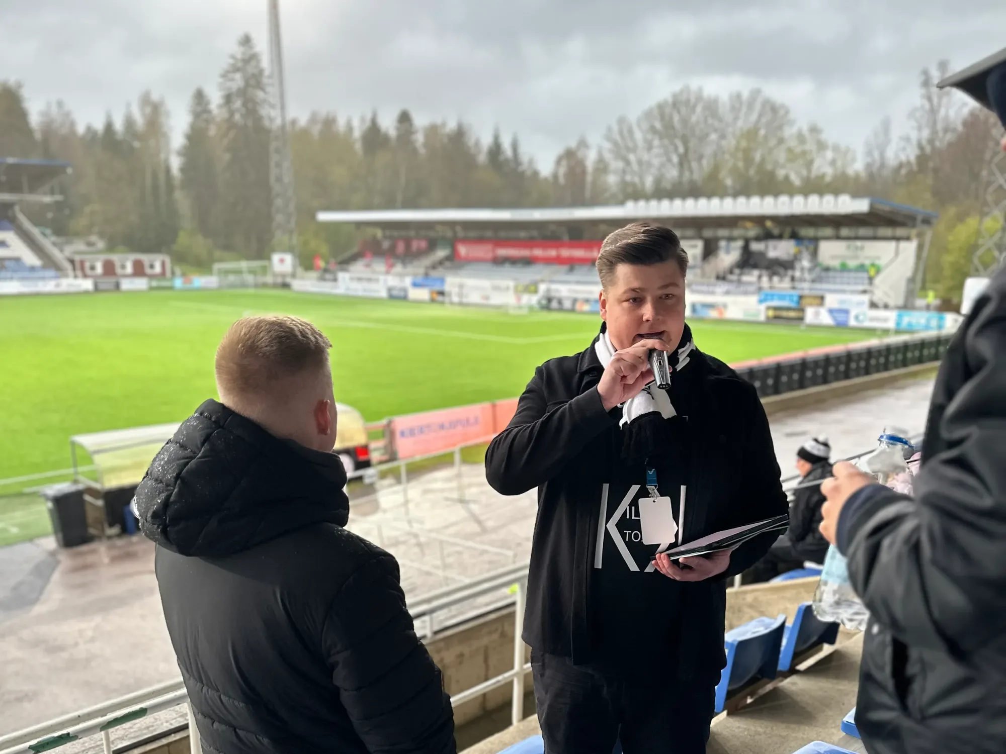 Eeli Arola juontaa mikrofoniin jalkapallostadionin katsomossa